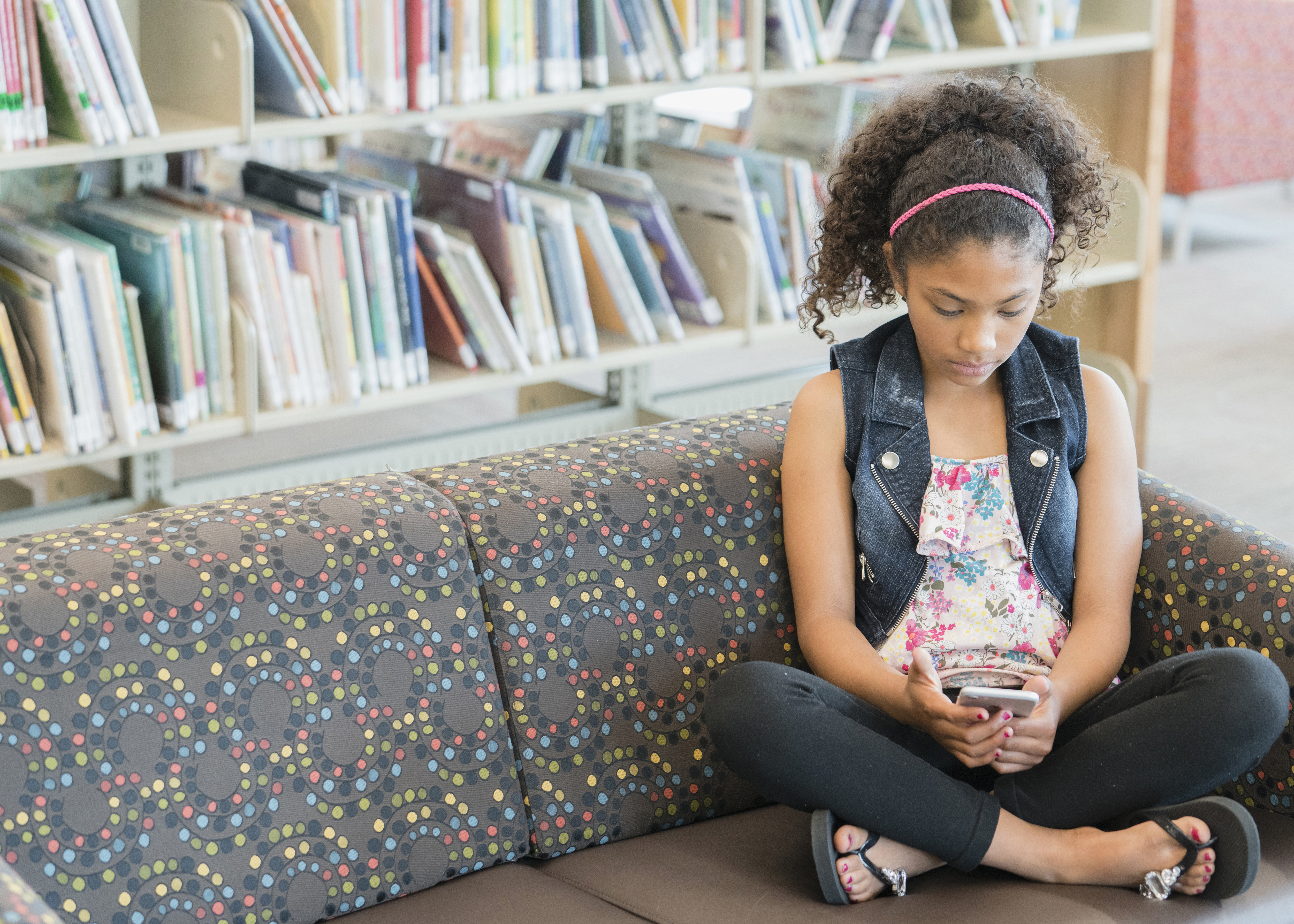 Serious mixed race girl on sofa in library texting on cell phone