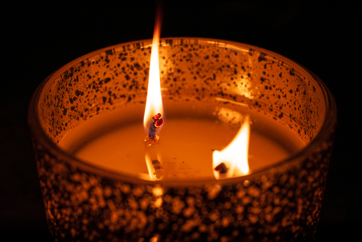 Twin flame burning candle with a warm orange glow in a speckled metallic holder against a dark black background